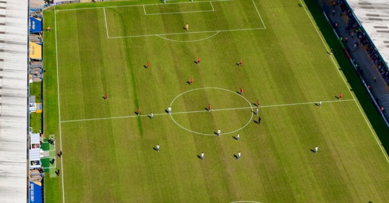 Aerial view of a football match in a sunlit stadium in Manchester.