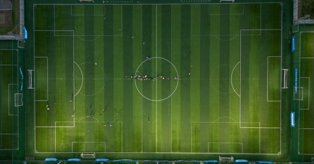 Top-down view of a soccer field with players during a daytime match.