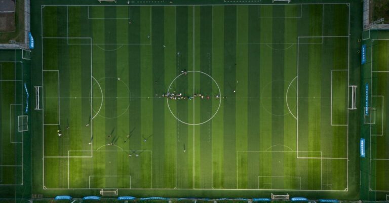 Top-down view of a soccer field with players during a daytime match.