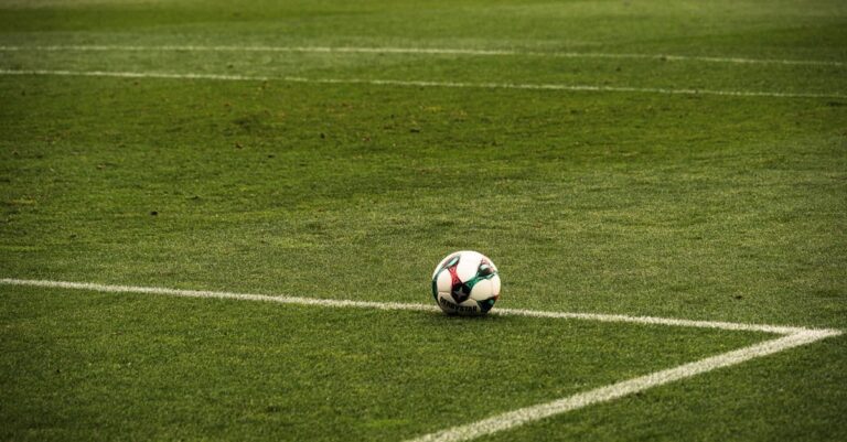A soccer ball rests on a well-maintained green football field corner, ready for play.